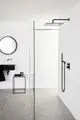 Moderne Duschsituation mit einer großen, gläsernen Duschabtrennung, einer Regendusche und einem schwarzen Waschbecken. Ideal Standard Produkte sind im Raum integriert.